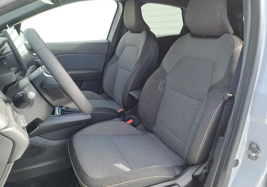 Vue intérieure côté conducteur du Renault Captur 2025, sièges tissu gris foncé avec surpiqûres jaunes et volant noir.