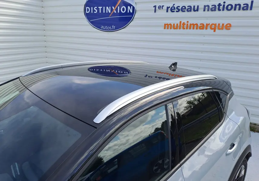 Vue plongeante sur le toit noir brillant et la carrosserie gris rafale métal du Renault Captur hybride 2025 avec barres de toit argentées.