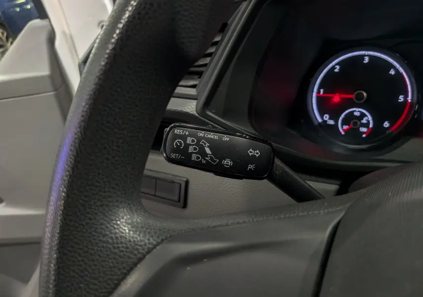 Gros plan sur le commodo de régulateur de vitesse du Volkswagen Transporter 6.1, tableau de bord et volant noirs visibles.