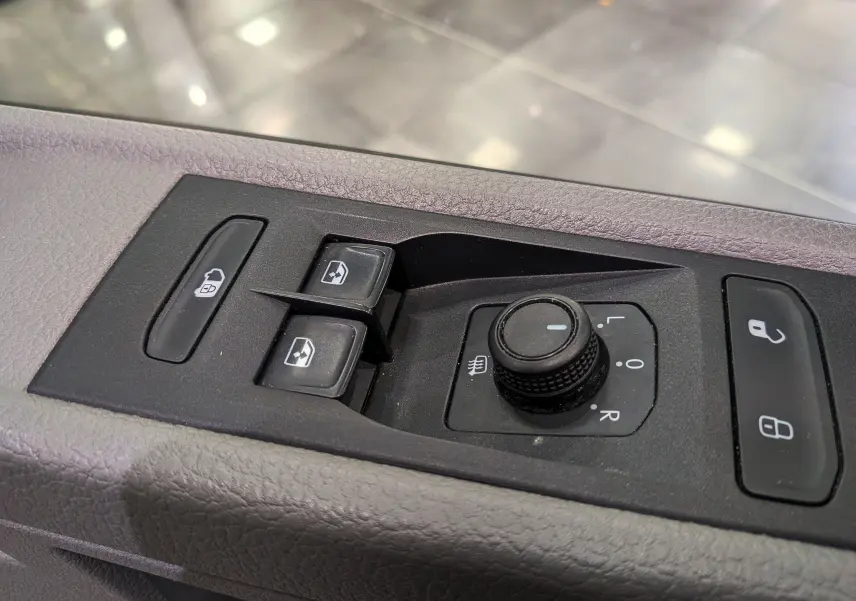 Gros plan sur les commandes de porte côté conducteur du Volkswagen Transporter 6.1 blanc, avec boutons de vitres et réglage des rétroviseurs.