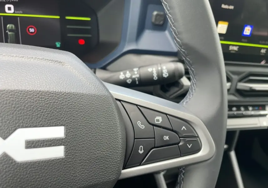 Gros plan sur le volant cuir gris du Dacia Bigster 2025 avec commandes multifonctions et tableau de bord numérique.
