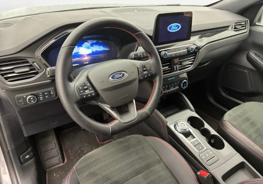 Vue intérieure côté conducteur du Ford Kuga 2024 gris, volant multifonctions, écran tactile et console centrale avec molette.