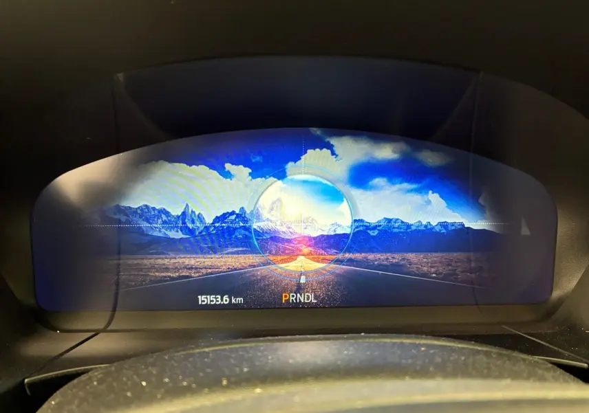 Vue du tableau de bord numérique du Ford Kuga 2024, affichant un paysage montagneux coloré et l'indicateur de boîte automatique.