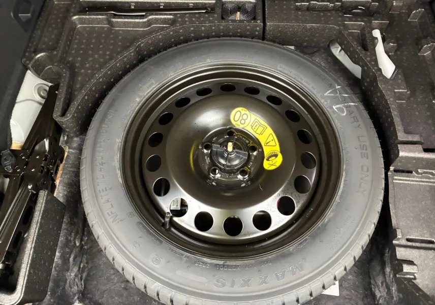 Pneu de secours noir avec jante acier vue de dessus dans le coffre d'un Ford Kuga gris 2024 hybride.