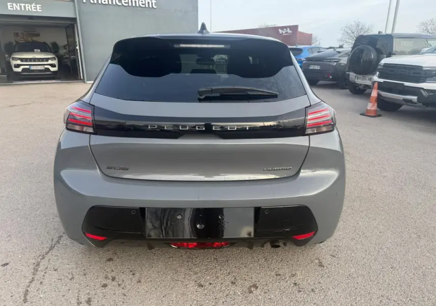 Vue arrière d'une Peugeot 208 Hybrid gris 2025 avec feux LED et lunette arrière teintée, stationnée en extérieur.