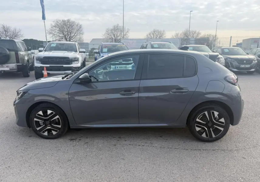 Vue de profil côté gauche d'une Peugeot 208 Hybrid 110 gris métallisé avec jantes alliage 16 pouces, en extérieur sur parking.