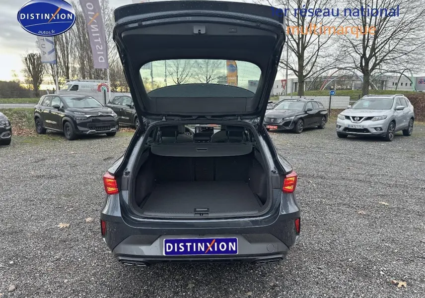 Vue arrière d'une CUPRA LEON ST gris magnétique avec coffre ouvert, feux arrière LED allumés, sur parking extérieur.