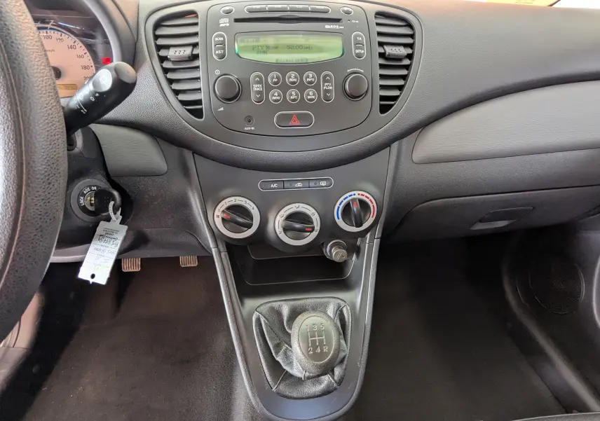 Vue intérieure centrée sur la console centrale et levier de vitesse manuelle d'une Hyundai i10 gris clair de 2010.