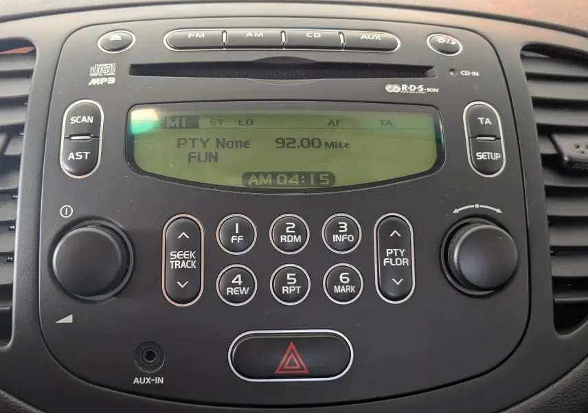 Gros plan sur la console centrale noire de la Hyundai i10 gris clair 2010, affichant la radio FM à 92 MHz.