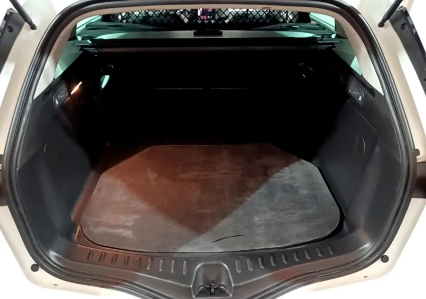 Coffre ouvert vu de l'arrière d'une Renault Mégane blanche 2023, espace de chargement vide avec tapis noir.