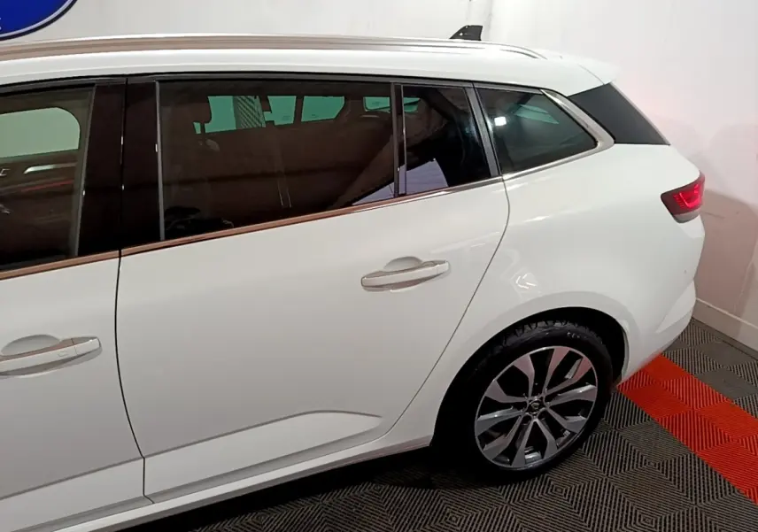 Vue latérale droite d'une Renault Mégane blanche, mettant en valeur la porte arrière et la roue arrière avec jante design.