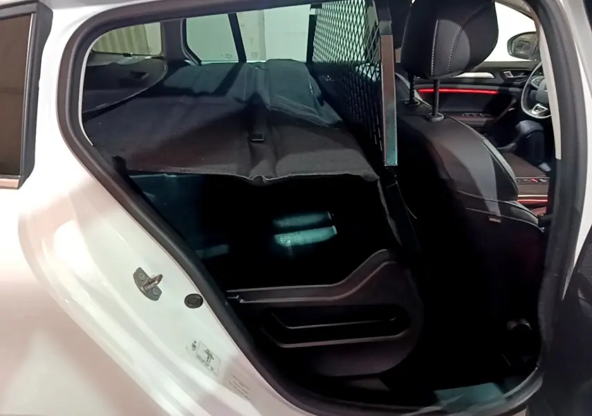 Vue intérieure côté arrière gauche de la Renault Mégane Techno TCe 140 blanche, avec séparation grillagée et banquette rabattue.