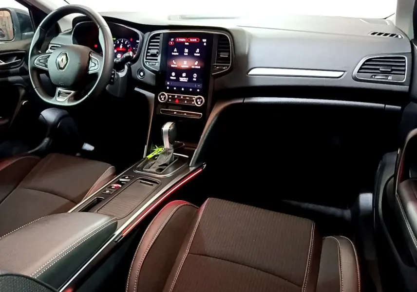 Vue intérieure avant droite de la Renault Mégane Techno TCe 140 2023, avec écran tactile central et éclairage d’ambiance rouge.