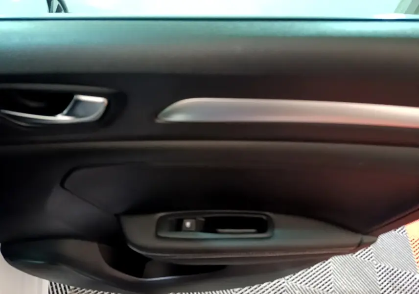 Gros plan sur la porte intérieure côté gauche de la Renault Mégane blanche, avec poignée argentée et commande de vitre noire.