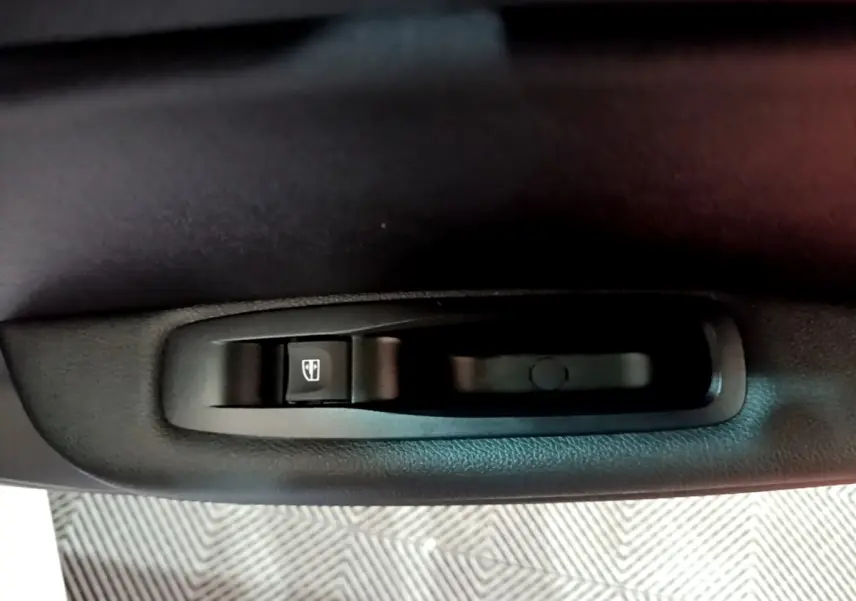 Gros plan sur la commande de lève-vitre électrique noire côté porte intérieure d’une Renault Mégane blanche.
