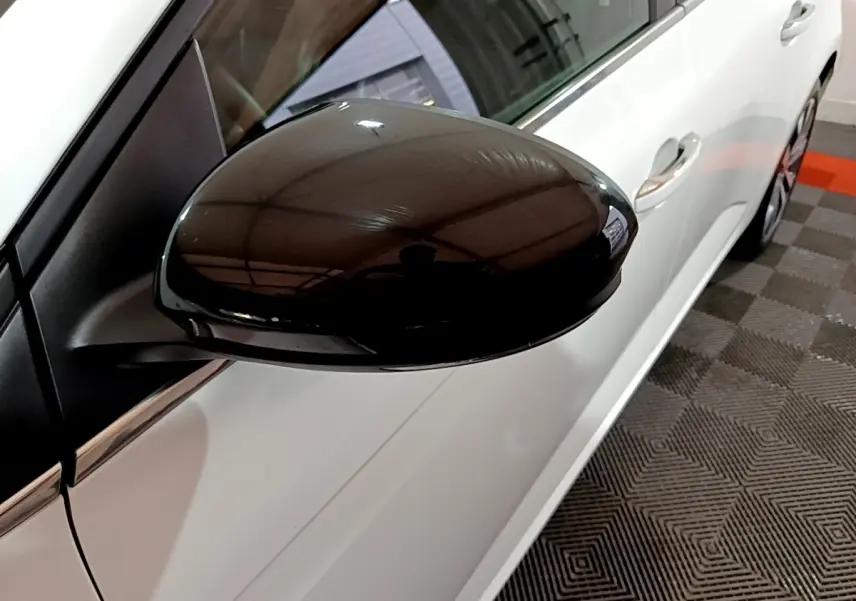 Gros plan sur le rétroviseur noir côté conducteur d’une Renault Mégane blanche vue de profil gauche.