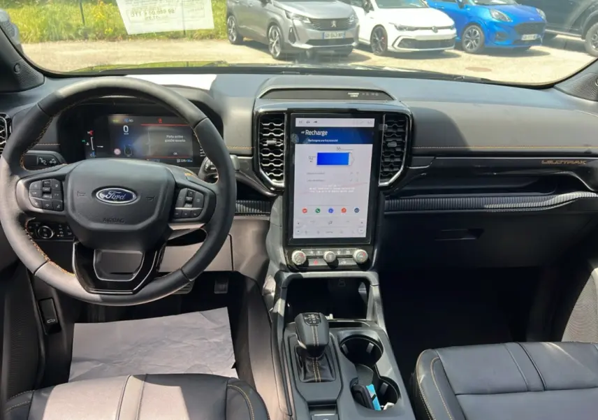 Intérieur du Ford Ranger PHEV 2025 vu de face, tableau de bord noir avec écran tactile vertical et volant cuir multifonctions.