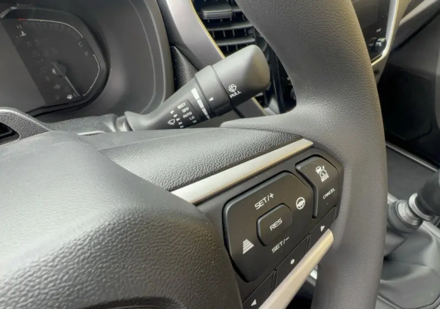 Gros plan sur le volant multifonctions noir de l'Isuzu D-MAX 2026 avec commandes de régulateur et boîte manuelle visible.