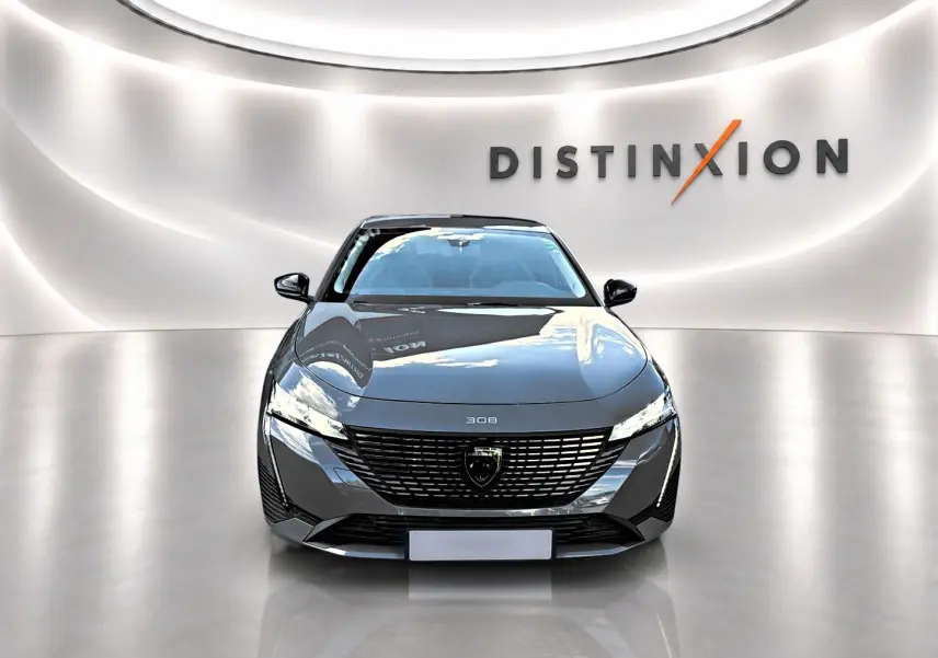 Vue frontale d'une Peugeot 308 gris selenium 2025, avec calandre noire et phares LED fins dans un showroom lumineux.
