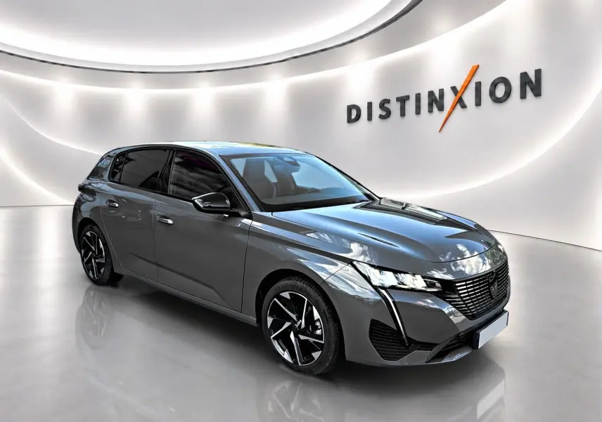 Peugeot 308 gris selenium en 3/4 avant droit, avec jantes alliage noires et phares LED distinctifs.