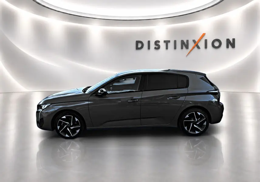 Profil droit d'une Peugeot 308 gris selenium 2025 dans un showroom lumineux avec jantes alu noires et logo Distinxion en arrière-plan.