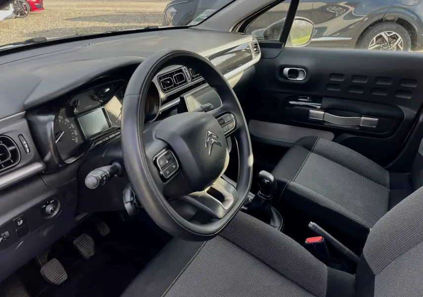 Intérieur de la Citroën C3 blanche 2019, vue côté conducteur montrant volant, tableau de bord et siège avant noir.