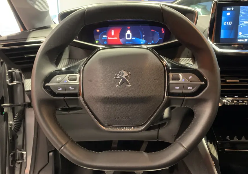 Vue rapprochée du volant noir de la Peugeot 208 PureTech 100 Allure Business avec tableau de bord numérique et écran GPS.