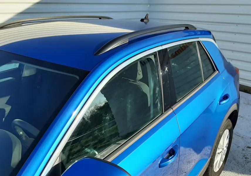 Vue 3/4 avant droit du Volkswagen T-Roc bleu 2022, mettant en valeur les rétroviseurs et barres de toit noires.