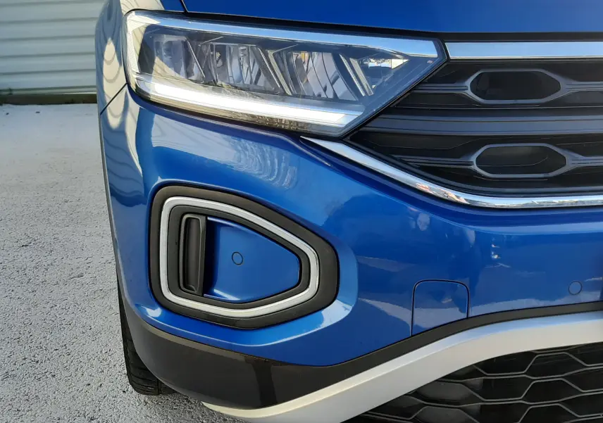 Gros plan sur l'avant gauche du Volkswagen T-Roc bleu 2022, mettant en valeur le phare LED et la calandre noire.