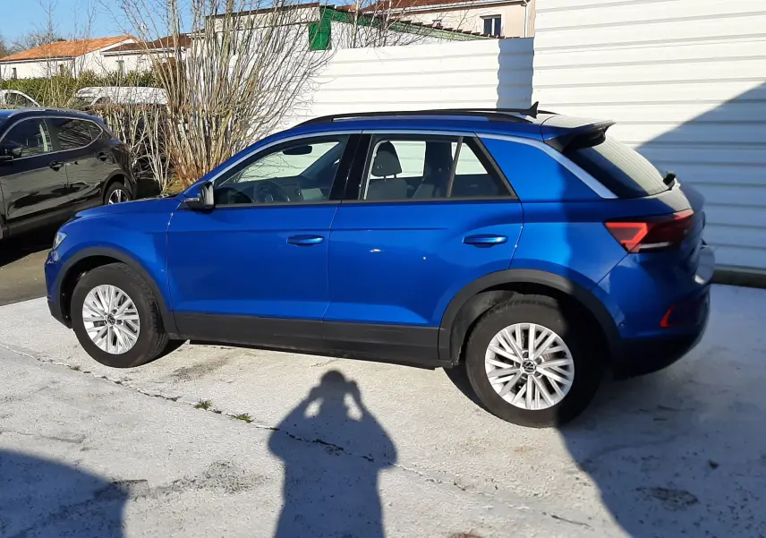 Volkswagen T-Roc bleu en vue de profil côté gauche, avec toit noir et jantes alliage, stationné en extérieur.