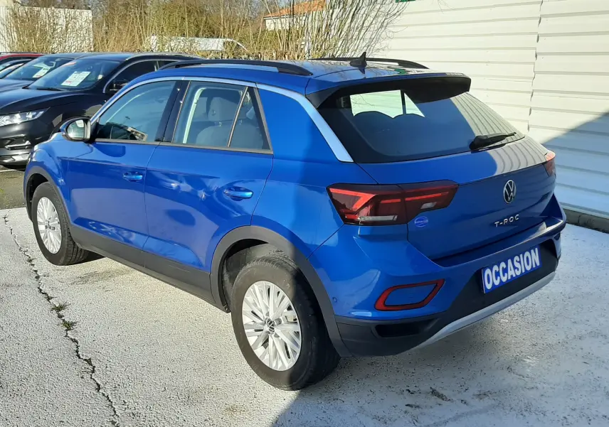 Vue 3/4 arrière droite d'un Volkswagen T-Roc bleu 2022, avec toit noir et feux arrière LED, sur parking extérieur.