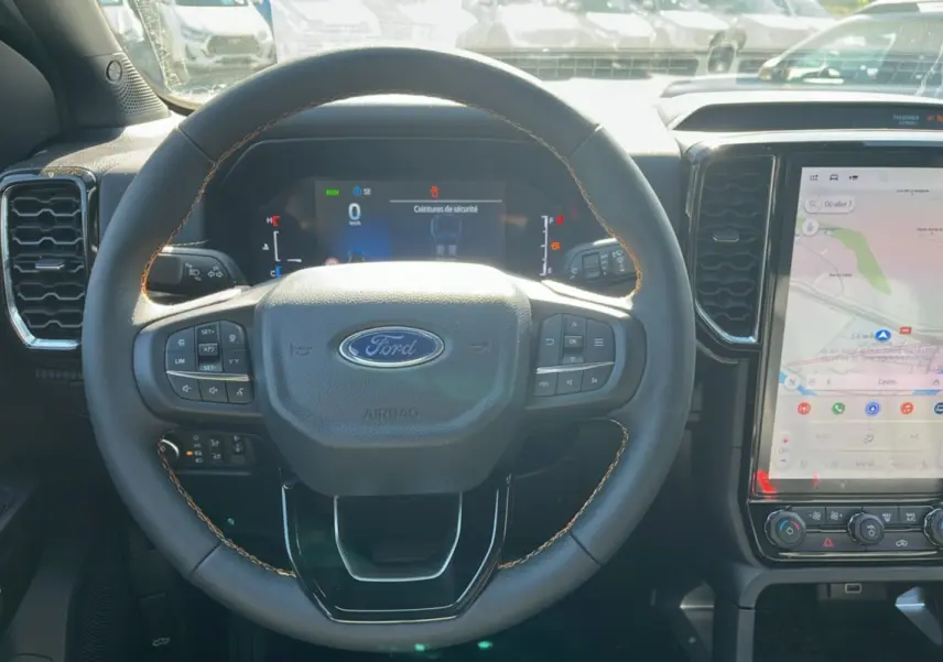 Vue intérieure centrée sur le volant cuir noir avec coutures marron et écran tactile vertical du Ford Ranger PHEV 2025.