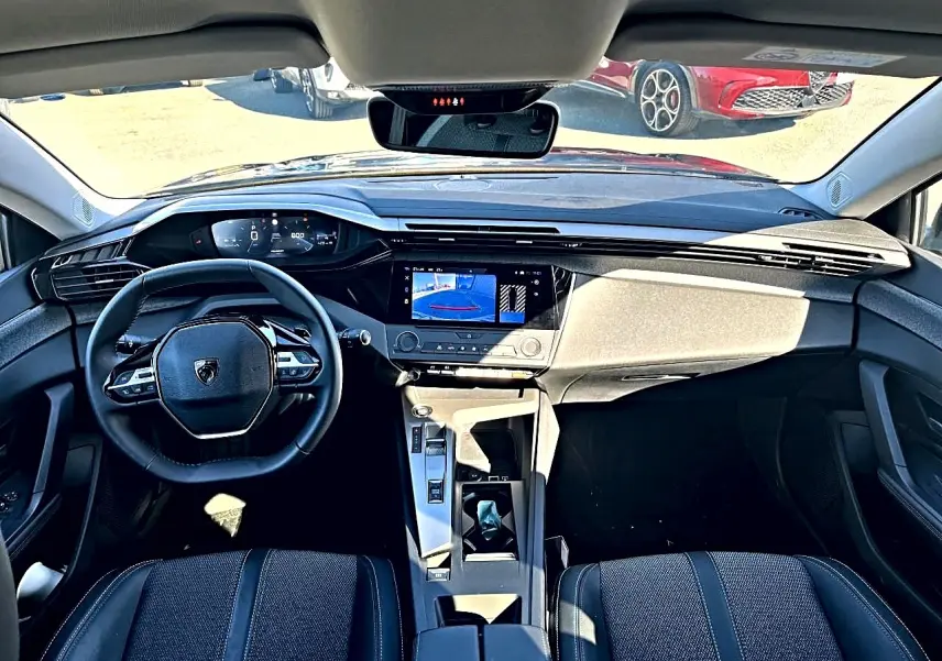 Vue intérieure avant de la Peugeot 308 noire, montrant le tableau de bord digital et l'écran tactile central avec caméra de recul.