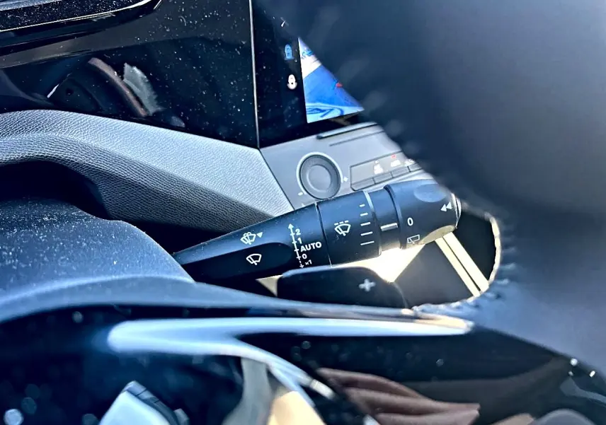Détail du commodo d’essuie-glace et partie du volant noir dans l’habitacle d’une Peugeot 308 noire 2025.