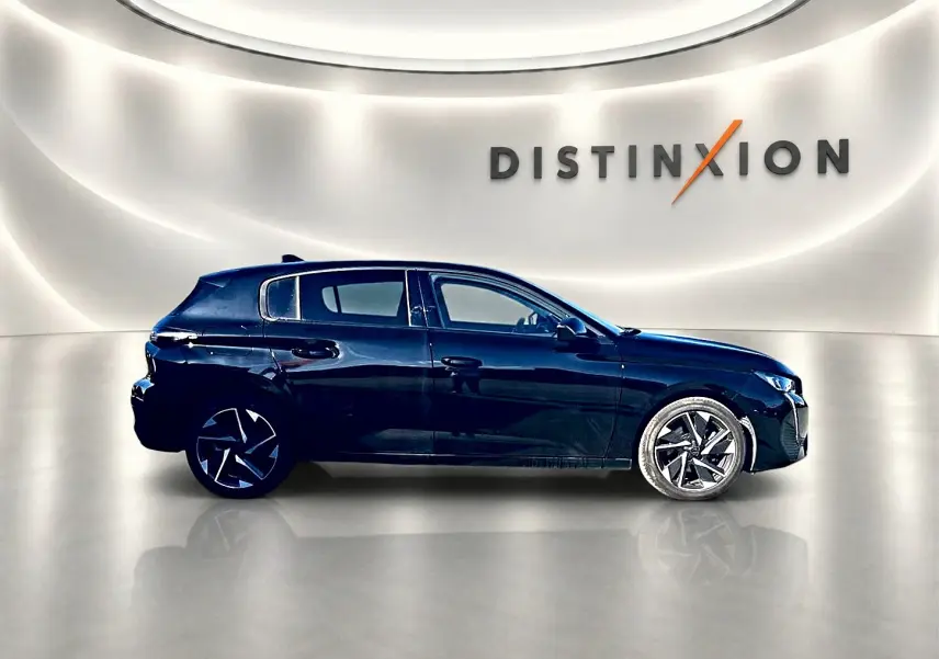 Profil droit d'une Peugeot 308 noire 2025 avec jantes alu stylisées, dans un showroom lumineux au mur blanc.