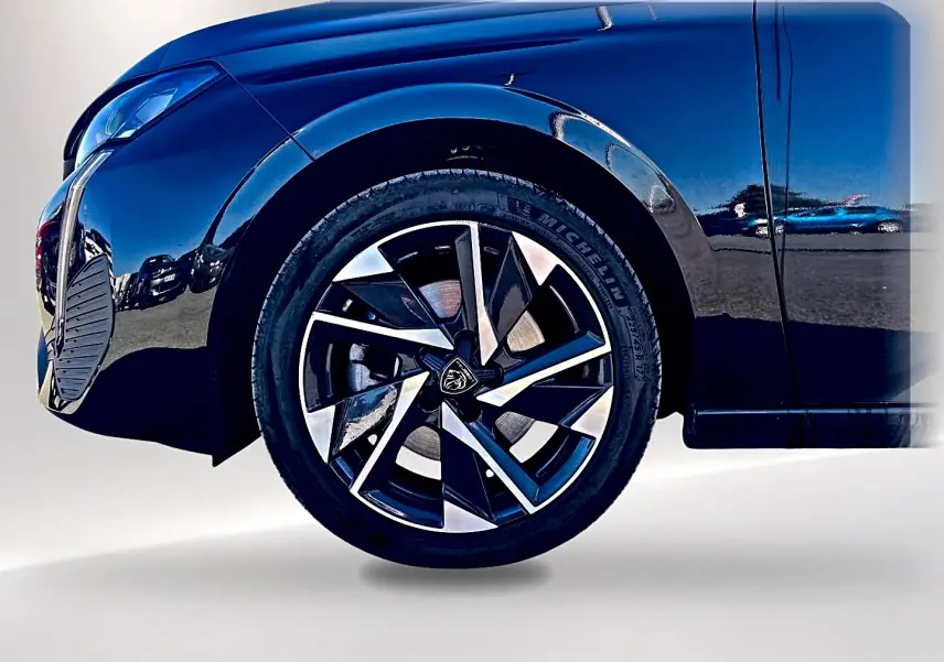 Gros plan sur la roue avant gauche noire d'une Peugeot 308 2025, mettant en valeur la jante alu au design moderne.