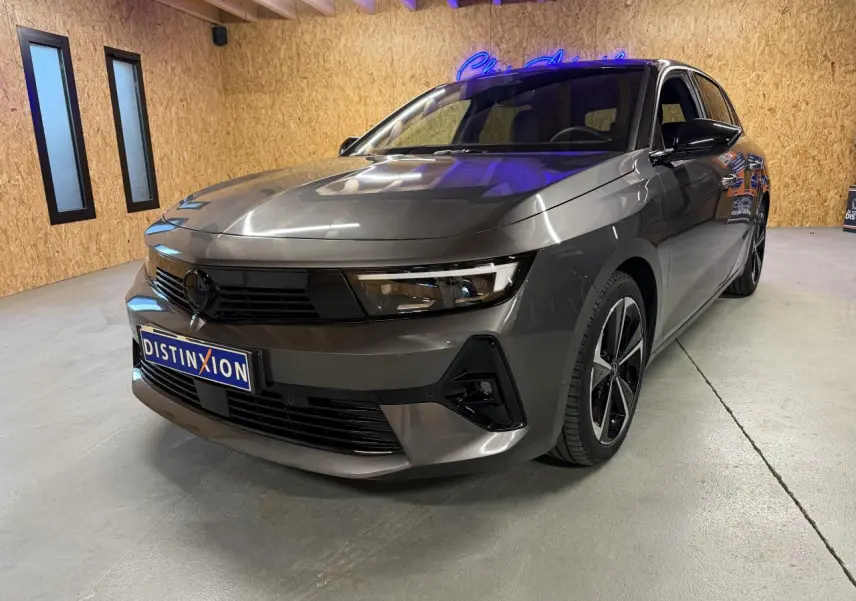Opel Astra gris foncé vue 3/4 avant droit en intérieur, avec calandre noire et jantes alliage 17 pouces.