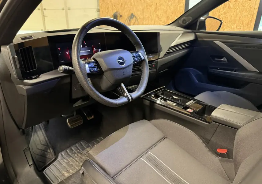 Intérieur avant droit de l’Opel Astra 2024, montrant le volant cuir, tableau de bord digital et sellerie tissu gris foncé.