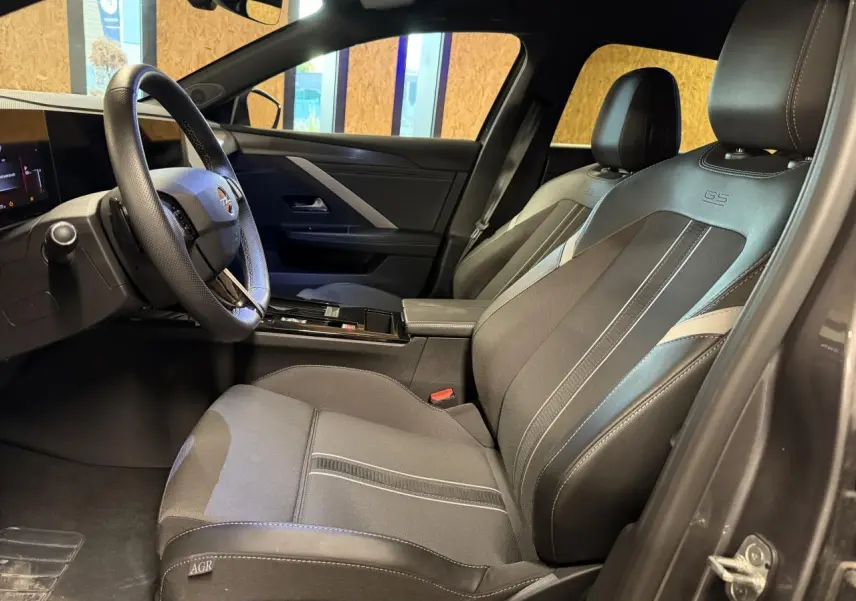 Vue intérieure côté conducteur de l’Opel Astra 2024 avec sièges mixte tissu/TEP noirs et volant cuir perforé.