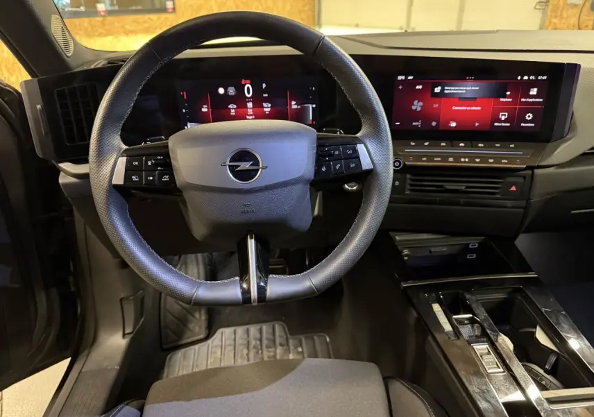 Vue intérieure de face du poste de conduite de l'Opel Astra 2024 avec volant cuir et écran tactile panoramique noir.