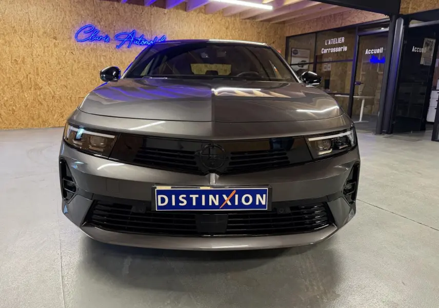 Vue frontale d'une Opel Astra gris foncé avec calandre noire et pare-chocs avant sportif dans un garage.