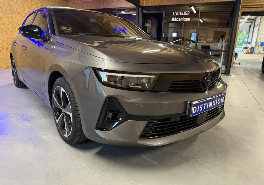 Opel Astra gris foncé vue 3/4 avant droit, calandre noire et jantes alliage 17 pouces diamantées.
