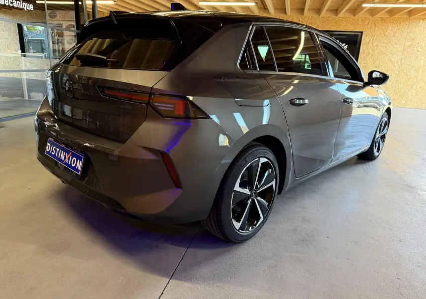 Vue 3/4 arrière droit d'une Opel Astra gris foncé avec toit noir et jantes alliage 17 pouces dans un garage.