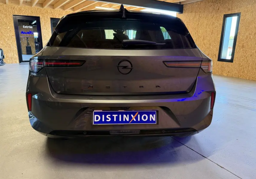Vue arrière d'une Opel Astra gris foncé avec logo noir et pare-chocs arrière noir dans un garage lumineux.