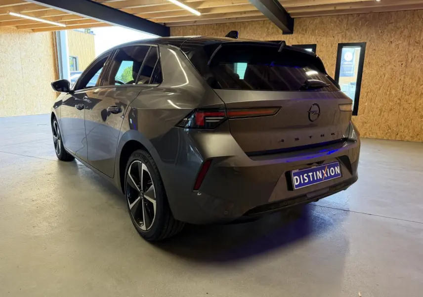 Vue 3/4 arrière droite de l'Opel Astra gris foncé avec jantes alliage 17 pouces et toit noir Karbon dans un garage.