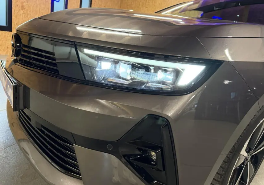 Gros plan sur l'avant droit d'une Opel Astra gris foncé avec phares LED et calandre noire brillante.