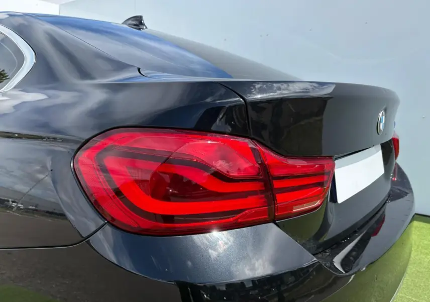 Feu arrière gauche en gros plan d'une BMW Série 4 Gran Coupé 420d noir saphir, reflet sur la carrosserie lisse.