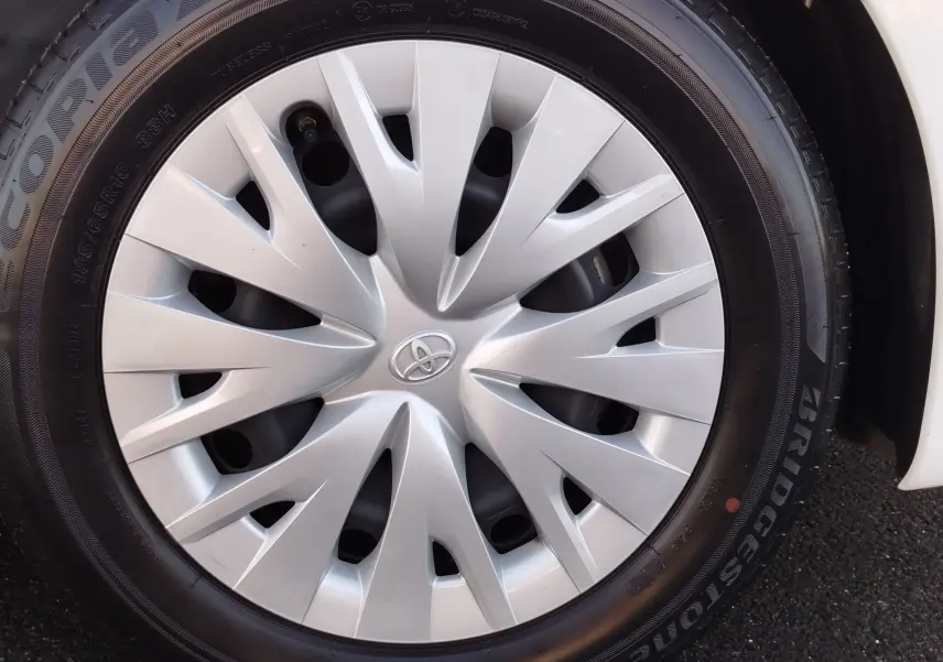 Gros plan sur la roue avant droite d'une Toyota Yaris blanche avec enjoliveur argenté au design étoilé.