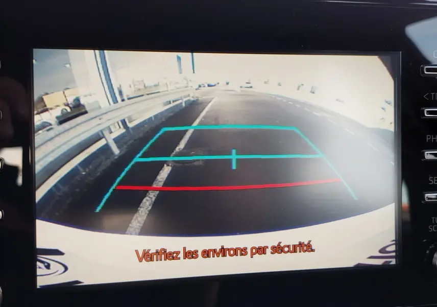 Vue de la caméra de recul d'une Toyota Yaris blanche, affichant les lignes de guidage sur un parking extérieur.