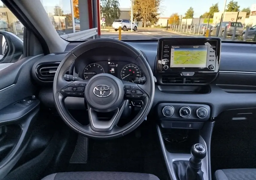 Vue intérieure avant de la Toyota Yaris blanche 2023, volant multifonction, écran tactile avec navigation et boîte manuelle.